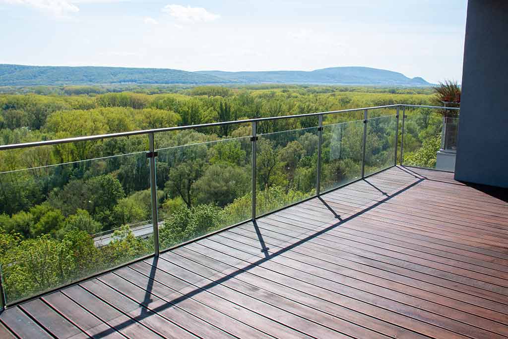 A deck with a glass railing overlooking trees
