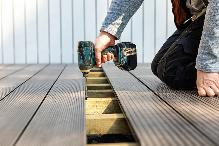 A person installing composite deck boards with a screwdriver