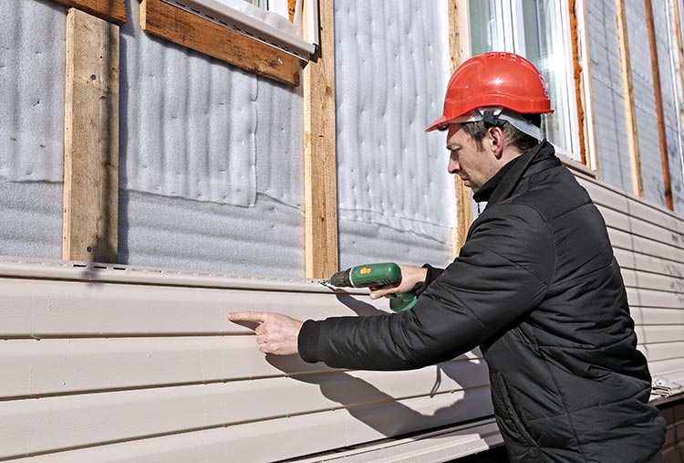 A worker nailing siding to a wall