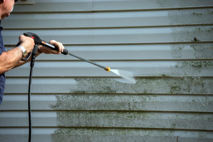 A person washing horizontal vinyl siding.