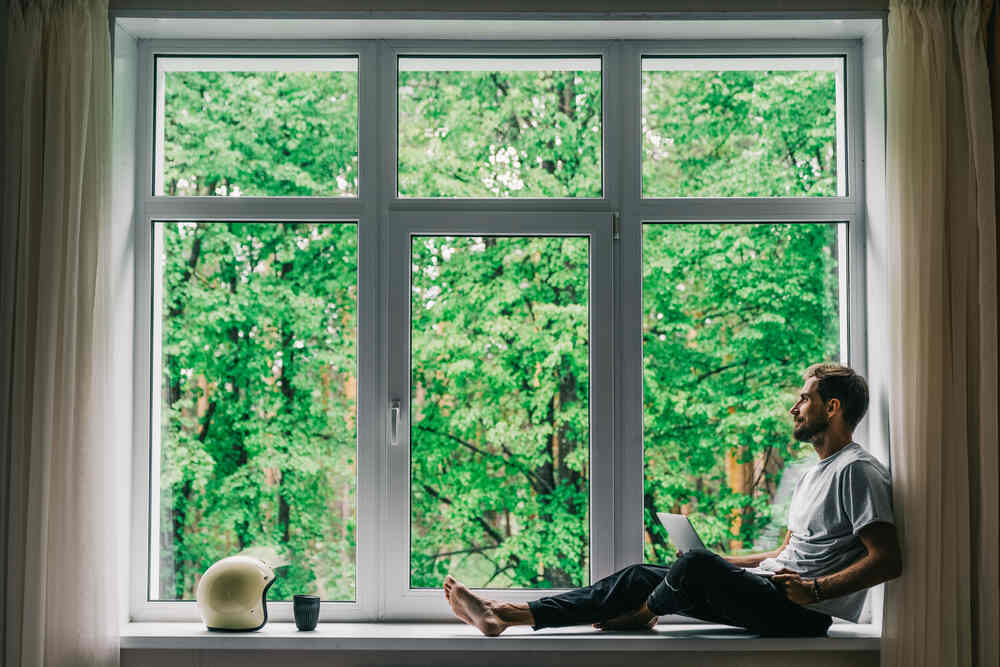 A man enjoying his casement windows with a view of trees.