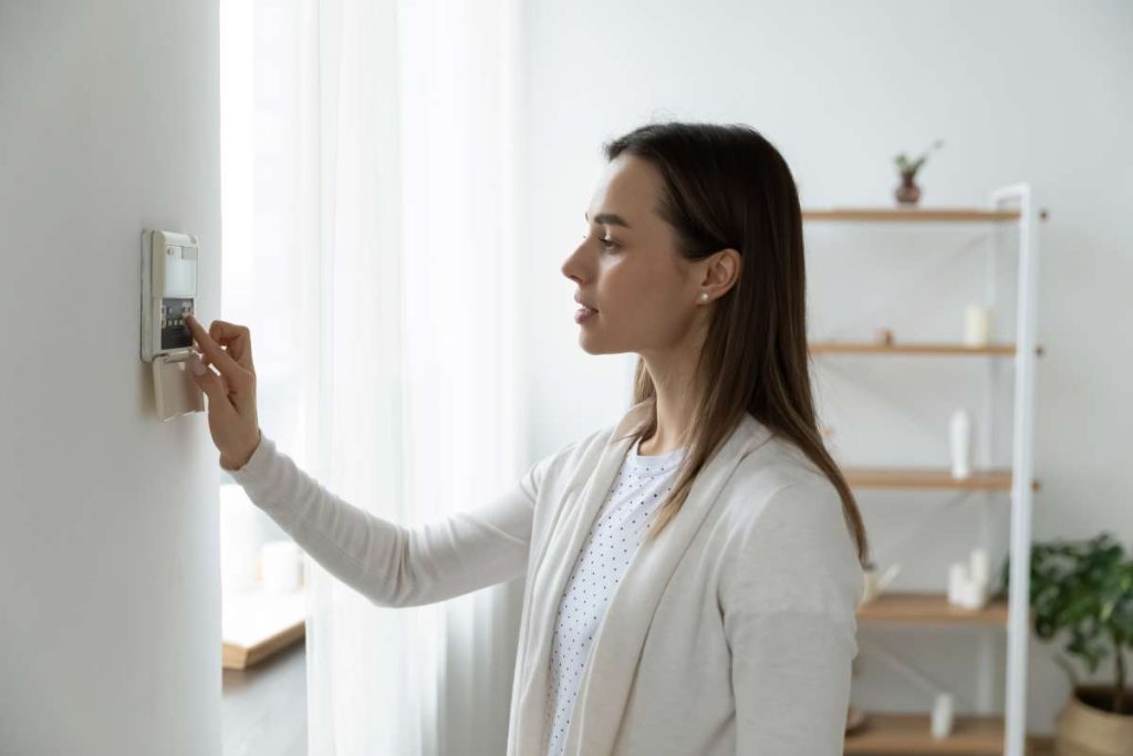 A woman adjusting a thermostat inside a house.