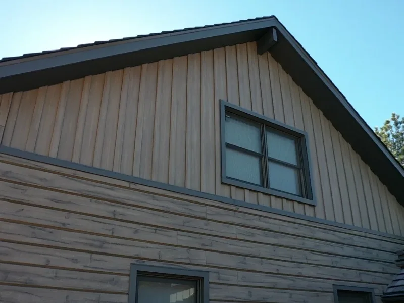 Modern home exterior with vertical siding on the upper level and horizontal siding on the lower level, with dark trim around the roof and windows.